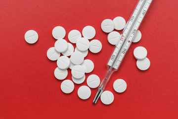 Thermometer and pills on red background.