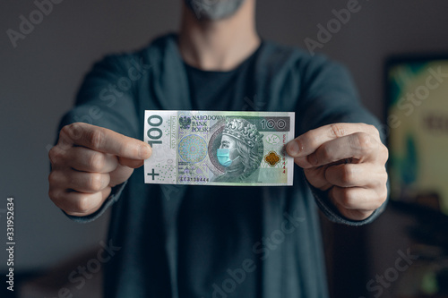 Man holds in hands 100 zlotych banknote  with a face mask against Corona virus infection. Global economy hit by covid19 outbreak and pandemic. Polish economy, health care, stock  reach the bottom