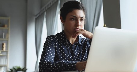 Focused young indian woman looking at computer monitor. Concentrated entrepreneur freelancer working remotely on laptop online at home office, solving problems. Serious student doing homework.