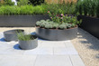 Moderne Garten- und Terrassengestaltung im Materialmix:Terrassen aus Steinplatten und Schotter sowie Metall Pflanzgefäße mit Gräsern und und blühenden Kübel Pflanzen	