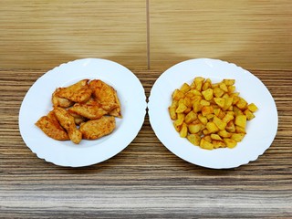 Fried chicken and fried potatoes on two white porcelain plates