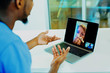 © Carlos David - Portrait of a sick patient coughing into tissue being helped via tele medicine by a male doctor wearing blue scrubs uniform using laptop