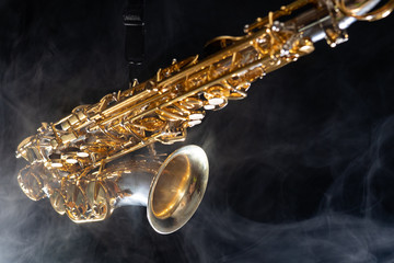 Golden shiny alto saxophone on black background with smoke. copy space