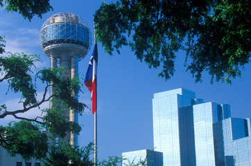 View of Reunion Tower and Hyatt Hotel in Dallas, TX through trees with state flag