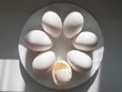 A group of white eggs and eggshells among them in a white plate, on a white wooden background, in the sun. The concept of superiority , success, exclusivity, a symbol of the birth of a new idea
