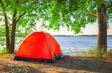 red tourist tent on lake in summer