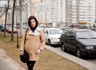 Photo portrait walk brunette girl in a beige coat in the city in sunny weather on the background of the road