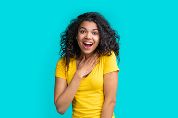 Wall Mural - Portrait of beautiful smiling dark skinned girl wearing bright colored yellow t-shirt isolated over blue background