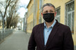 © andreysha74 - A middle- aged European in a protective disposable black medical mask in the city.