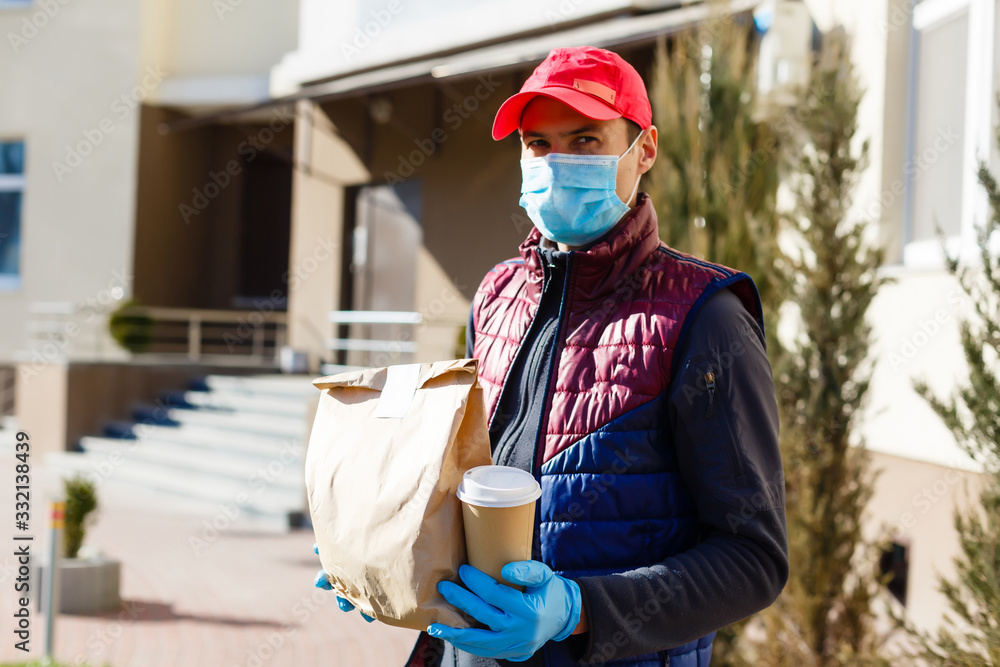Courier in protective mask and medical gloves delivers takeaway food. Delivery service under quarantine, disease outbreak, coronavirus covid-19 pandemic conditions. - obrazy, fototapety, plakaty 