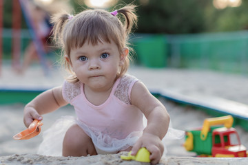 Cute toddler girl playing in sand on outdoor playground. Beautiful baby in red trousers having fun on sunny warm summer day. Child with colorful sand toys. Healthy active baby outdoors plays games