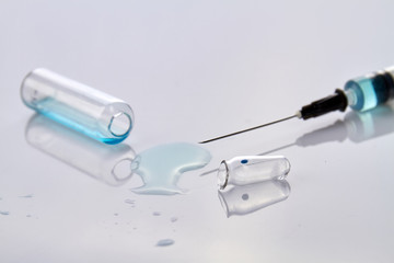 Close up syringe and opened vial ampoules. Spilled liquid on white reflective surface.