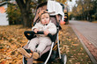 A beautiful little baby in a stroller outside in the fall