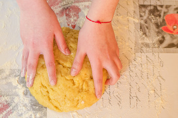 Female hands knead the dough for a sweet cake on a table sprinkled with flour. Making shortcrust pastry at home in the kitchen. Selective focus.