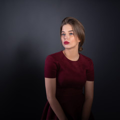 Leinwandbilder - Portrait of attractive young woman over gray background. Amazing girl with perfect makeup wearing elegant deep red dress. Beauty and fashion