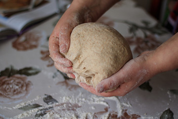 Female hands knead home made whole wheat bread. Dinkel flour bread kneading. Whole wheat bread made from spelled and rye flour. Woman's hands knead dough on a table  sprinkled with flour.