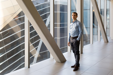 Portrait of a positive man near large office windows. A 35-40 year old man a blue shirt poses in the office back hallway against the background of a large window.