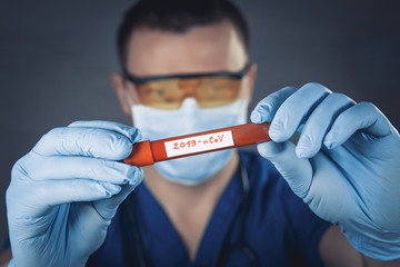 Doctor wearing respirator mask holding a positive blood test result for the new rapidly spreading Coronavirus. Doctor  holding test tube with blood for 2019-nCoV analyzing.