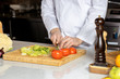 © Roman - cropped young cook man in white apron cutting vegetables on wooden cutting board, cooking tasty delicious dish in kitchen, cook use sharp knife for cutting