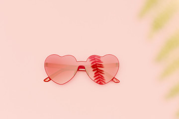 Wall Mural - Stylish heart shaped glasses with shadow from palm leaves on pink background with copy space. Beautiful trendy red sunglasses. Fashion summer concept. Top view.