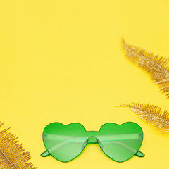 Wall Mural - Flat lay with fashion glasses green colored and golden palm leaves on yellow paper. Heart shaped eyeglasses. Trendly summer background with copy space.