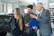 © Minerva Studio - Happy young family talking to the salesman and choosing their new car in a showroom