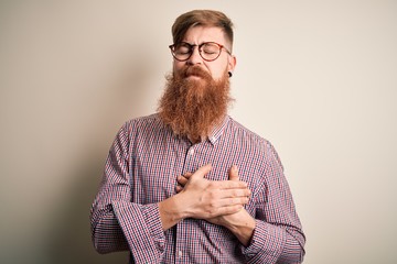 Canvas Print - Handsome Irish redhead business man with beard wearing glasses over isolated background smiling with hands on chest with closed eyes and grateful gesture on face. Health concept.