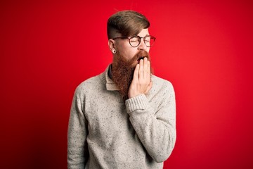 Canvas Print - Handsome Irish redhead man with beard wearing casual sweater and glasses over red background bored yawning tired covering mouth with hand. Restless and sleepiness.