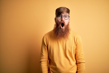 Wall Mural - Handsome Irish redhead man with beard wearing glasses over yellow isolated background afraid and shocked with surprise and amazed expression, fear and excited face.