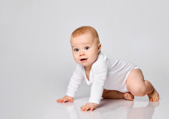 Wall Mural - Chubby ginger little one in bodysuit, barefoot. He is sitting on floor isolated on white studio background. Close up, copy space