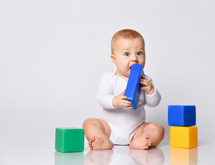 Wall Mural - Baby boy in bodysuit, barefoot. He is playing with multi-colored toys, sitting on floor isolated on white. Close up, copy space