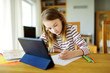 © MNStudio - Smart preteen schoolgirl doing her homework with digital tablet at home. Education and distance learning for kids. Homeschooling during quarantine.