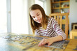 © MNStudio - Cute young girl playing puzzles at home. Child connecting jigsaw puzzle pieces in a living room table. Kid assembling a jigsaw puzzle. Fun family leisure.