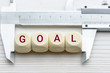 Measuring business goal setting / translate objectives into measurable goals concept : Vernier caliper and wood cubes with a word GOAL, depict tracking on progress or performance of a company targets