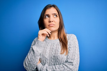 Sticker - Beautiful young woman wearing casual wool sweater standing over blue isolated background with hand on chin thinking about question, pensive expression. Smiling with thoughtful face. Doubt concept.