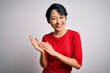 © Krakenimages.com - Young beautiful asian girl wearing casual red t-shirt standing over isolated white background clapping and applauding happy and joyful, smiling proud hands together