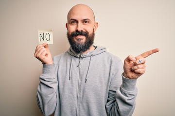 Sticker - Handsome bald man with beard holding reminder paper with negative message very happy pointing with hand and finger to the side