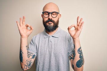 Wall Mural - Handsome bald man with beard and tattoo wearing casual polo and glasses relax and smiling with eyes closed doing meditation gesture with fingers. Yoga concept.