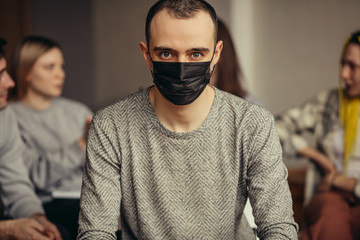 caucasian man put on medical mask so as not to infect other people with coronavirus, he sit with healthy people in isolated room. flu, influenza, virus, covid-19, coronavirus, global problem concept