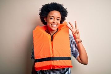 Young African American afro woman with curly hair wearing orange protection lifejacket showing and pointing up with fingers number three while smiling confident and happy.