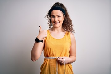 Sticker - Young beautiful woman with curly hair controlling weight using tape mesure happy with big smile doing ok sign, thumb up with fingers, excellent sign