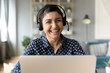 © fizkes - Head shot portrait smiling Indian woman wearing headphones posing for photo at workplace, happy excited female wearing headset looking at camera, sitting at desk with laptop, making video call