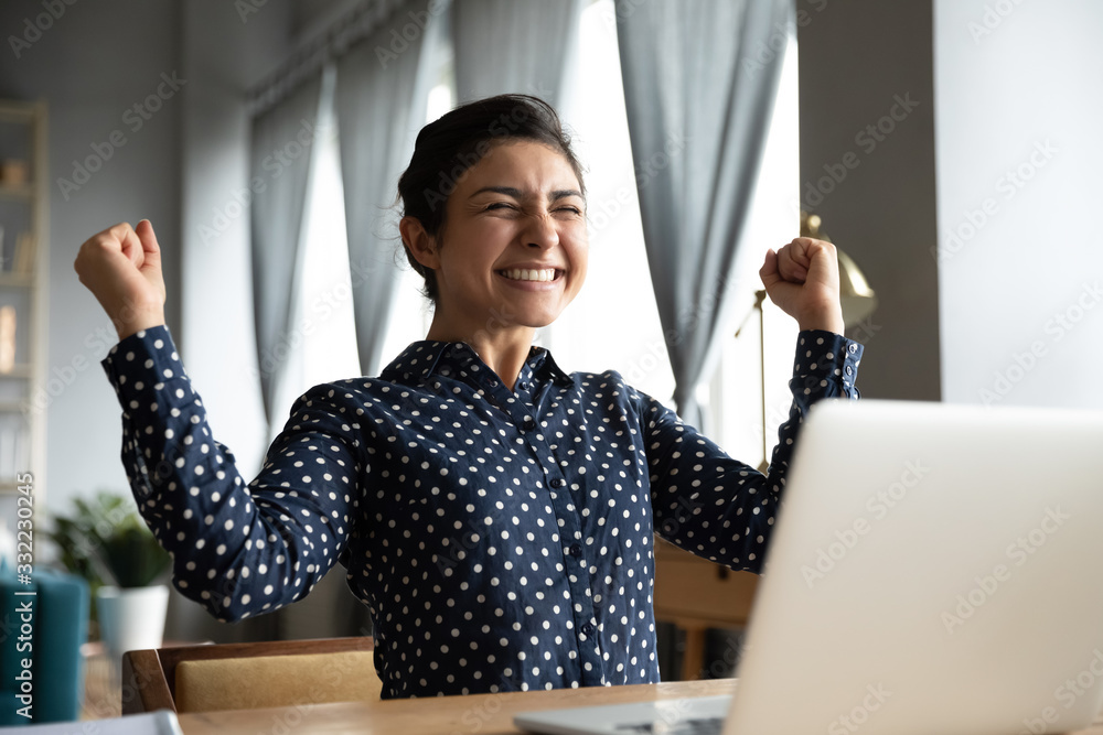 Smiling Indian woman excited by good news, work success, received great shopping or job offer, successful exam results, happy girl showing yes gesture, celebrating win, sitting at desk with laptop - obrazy, fototapety, plakaty 