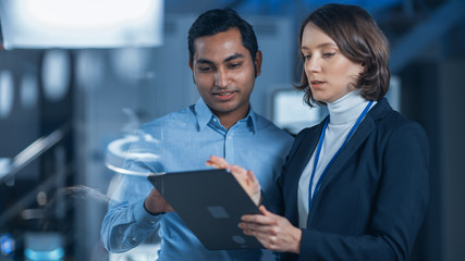 Poster - In Technology Research Facility: Female Project Manager Talks With Chief Engineer, they Consult Tablet Computer. Team of Industrial Engineers, Developers Work on Engine Design Using Computers