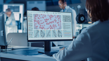 Poster - Over the Shoulder Shot: Female IT Scientist Uses Computer Showing System Monitoring and Controlling Program. In the Background Technology Development Laboratory with Scientists, Engineers Working