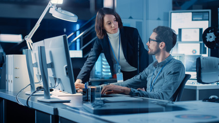 Fototapete - Futuristic Machine Engine Development Engineer Working on Computer at His Desk, Talks with Female Project Manager. Team of Professionals Working in the Modern Industrial Design Institution
