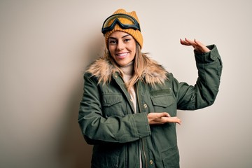 Canvas Print - Young brunette skier woman wearing snow clothes and ski goggles over white background gesturing with hands showing big and large size sign, measure symbol. Smiling looking at the camera. Measuring