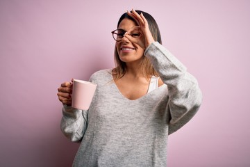 Canvas Print - Young beautiful brunette woman wearing glasses drinking pink mug of coffee with happy face smiling doing ok sign with hand on eye looking through fingers