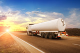 Fototapeta Sport - Big fuel tanker truck shipping fuel on the countryside road against a sky with a sunset