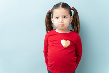 Wall Mural - Portrait of a cute little girl with ponytails pouting and looking sad against a blue background in a studio